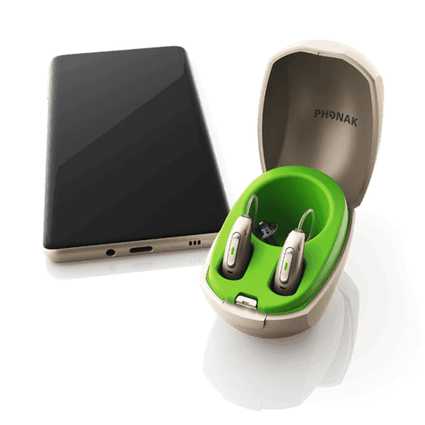 Par de aparelhos Phonak CROS no estojo carregador ao lado de um celular
