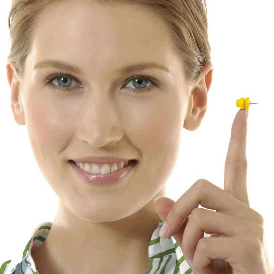 Mulher sorrindo com o pequeno aparelho auditivo Phonak Lyric na ponta do dedo