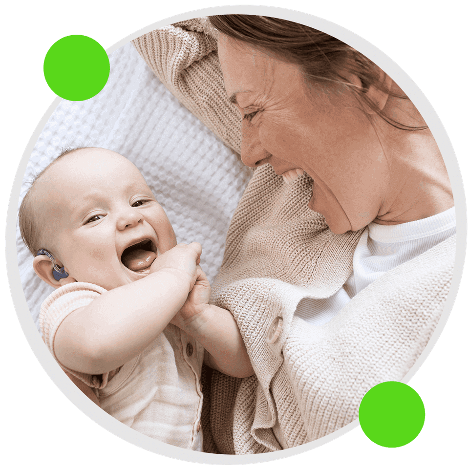Bebê sorrindo com aparelho auditivo, no colo da mãe